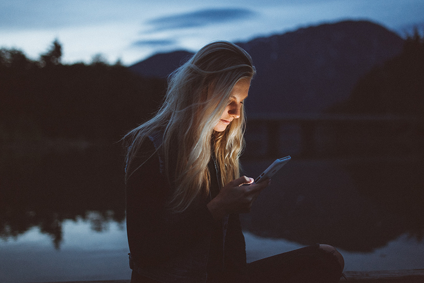 Women looking at personal alarm apps on her phone just after twilight by a lake.