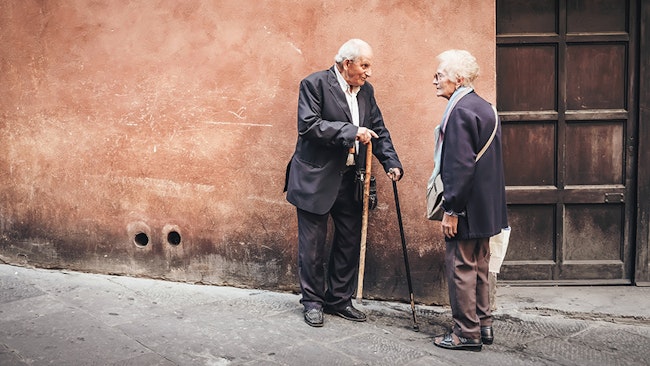 An old man and old woman talking on the street that might benefit from having personal alarms for the elderly.