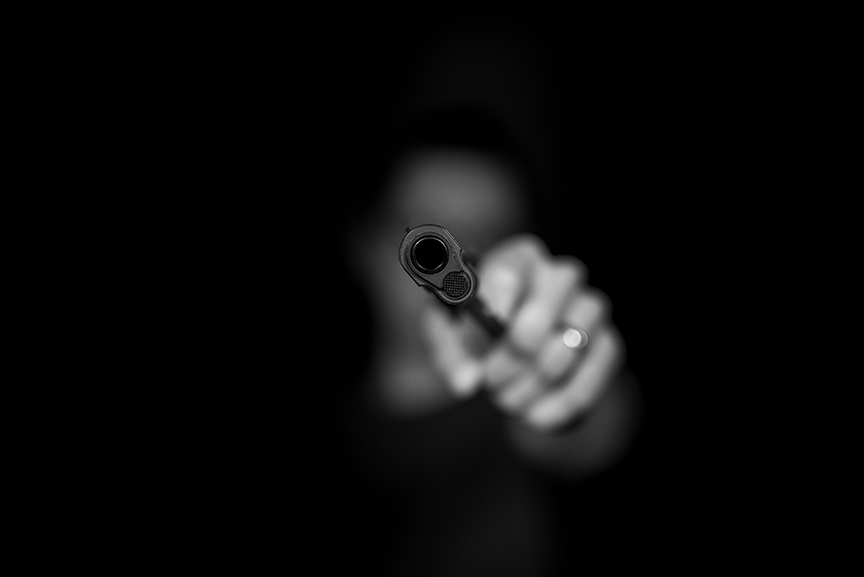 Violent Burglar Holding a gun at the camera with one hand. Burglars face is blurred.