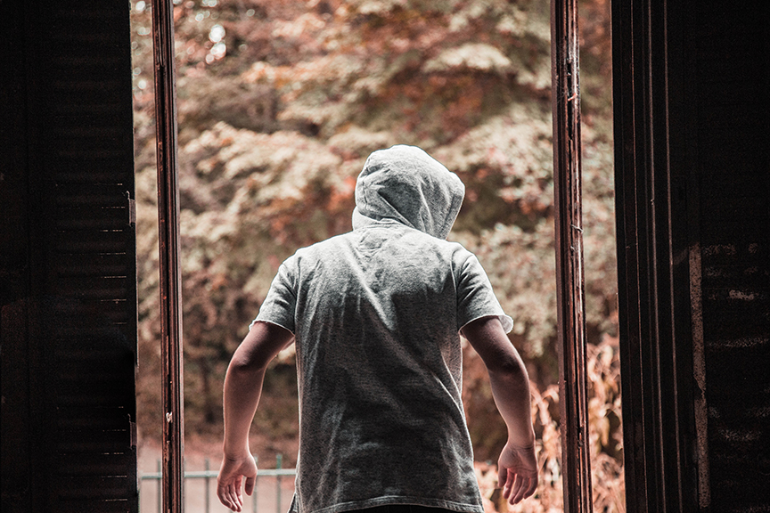 Burglar with hoody in middle of the day sneaking out of a house with his hood up.