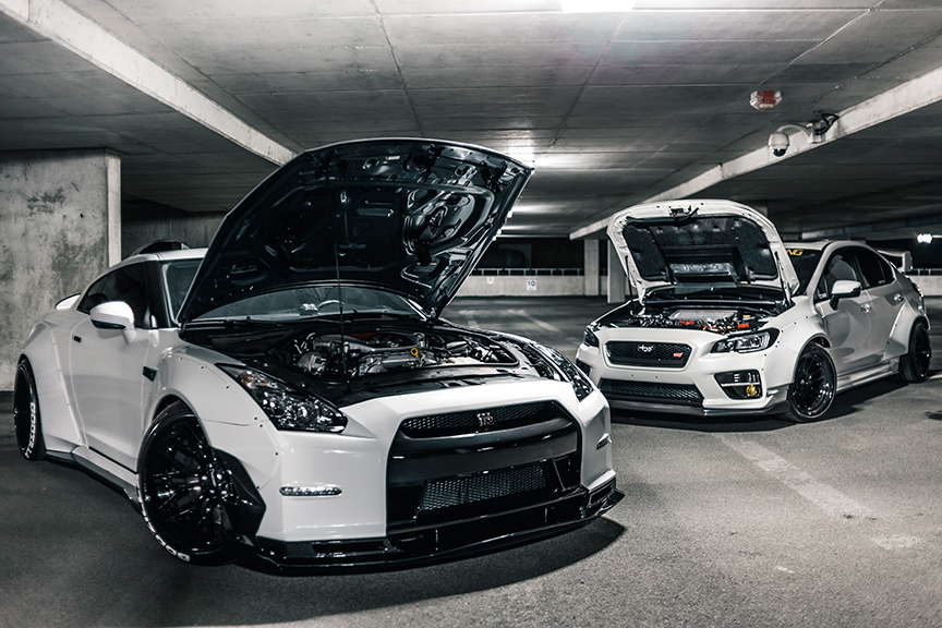 Two cars in a garage with the hoods up where anti theft tracking devices are placed. 