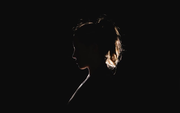 Silhouette of a woman being watched by a stalker in the darkness. 