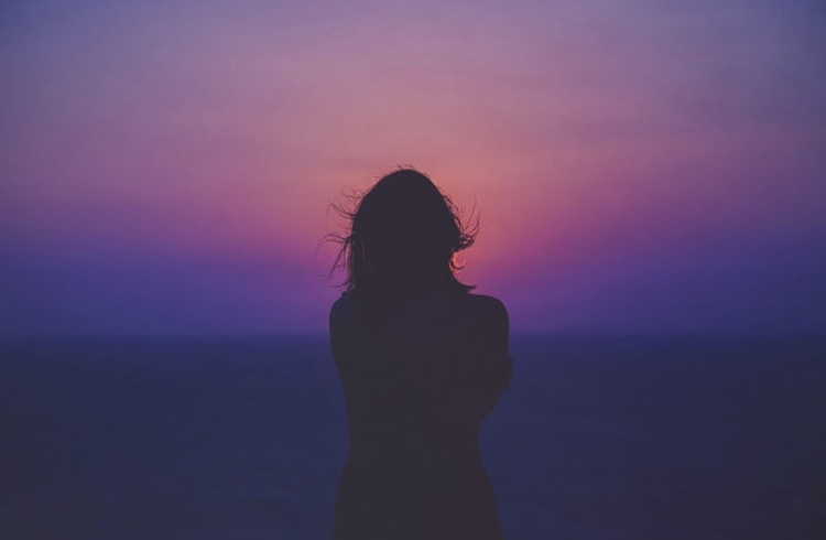 Viewpoint of the stalker looking at woman from behind that is watching the sunset.