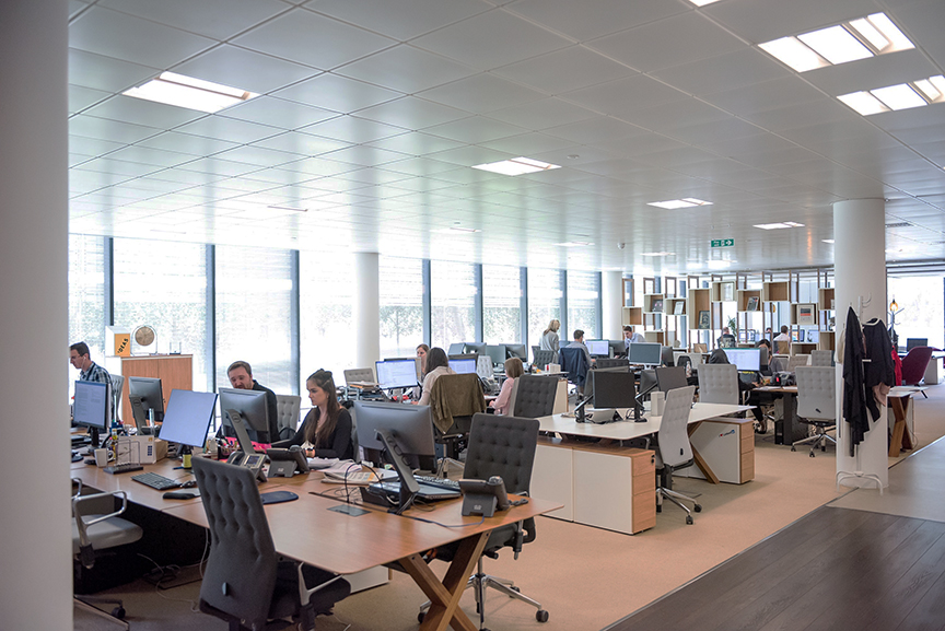 Office Floor of a Business where many employees sit at tables and desks working.