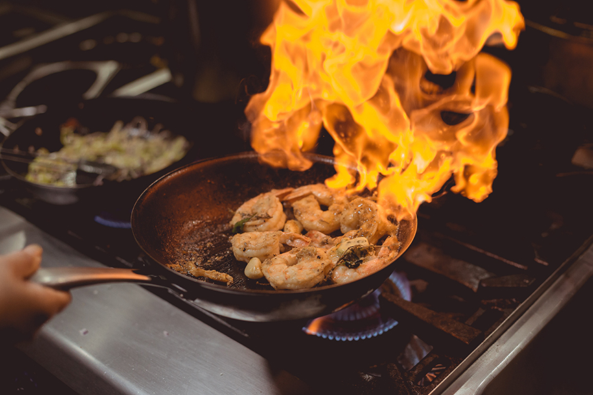Person cooking shrimp. The oil in the pan is on fire.