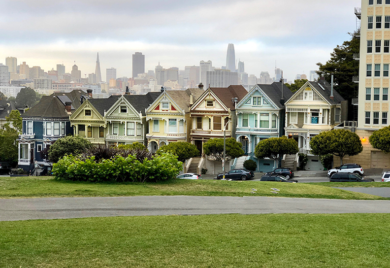 Several houses right next to each other with a view of the San Fransisco skyline behind it.