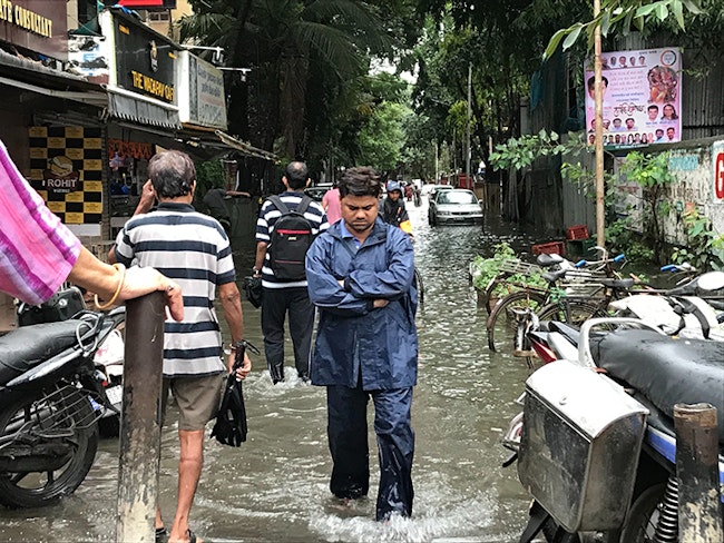 Man walking through crowded flooded street in a tropical area.