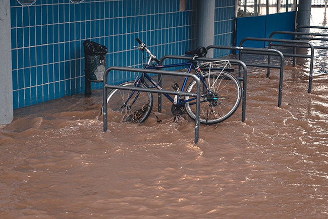 Bike chained to a bar, keeping  a flood of dirty water from carrying it away.