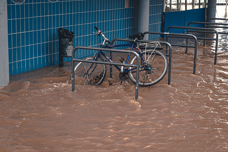 Bike chained to a bar, keeping a flood of dirty water from carrying it away.