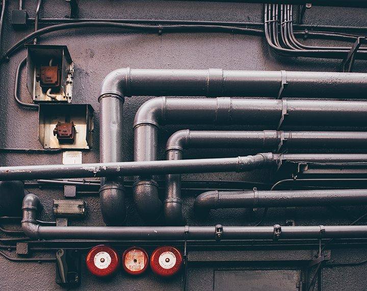Several different metal pipes going along and then inside of a building.