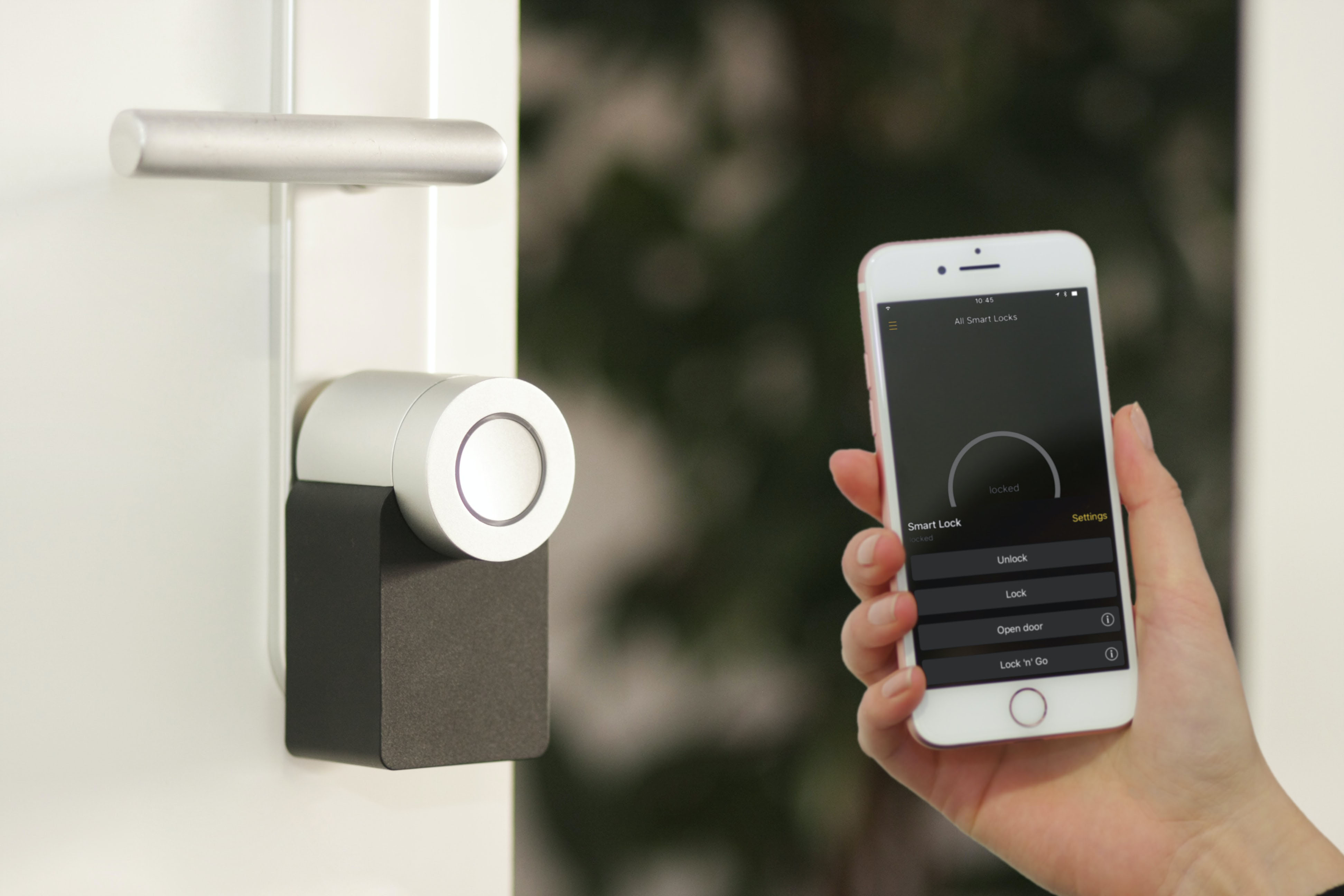 A hand holding a smartphone next to a smart lock on a white door.