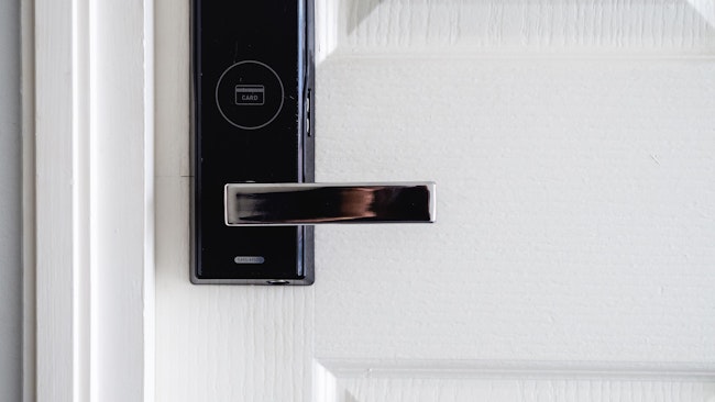 A metallic door handle with a smart lock on a white door.