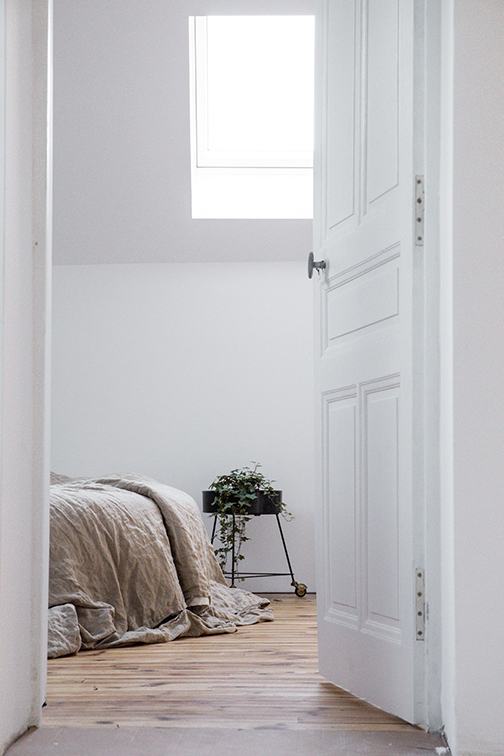 White unlocked bedroom door. Bed, plant, window, and wood flooring seen through the open door.
