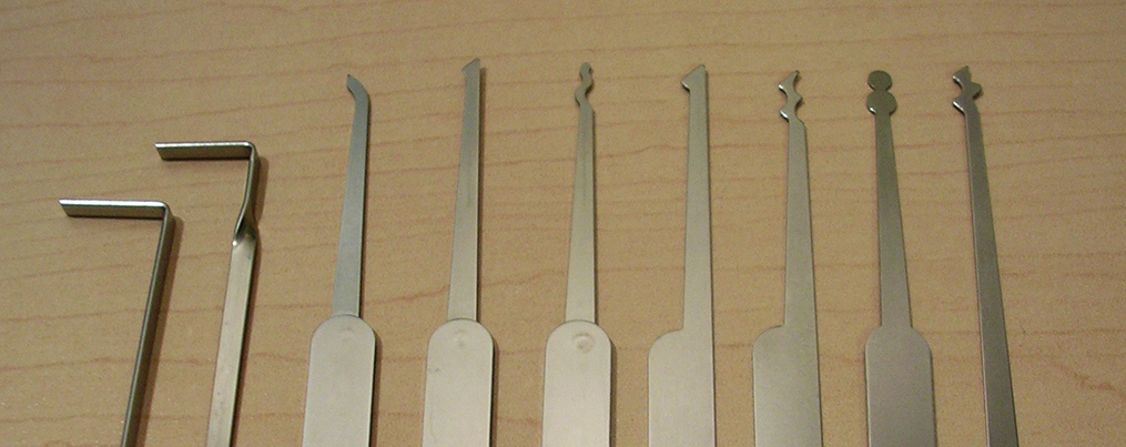 A set of lock-picking tools line up on a wood table.