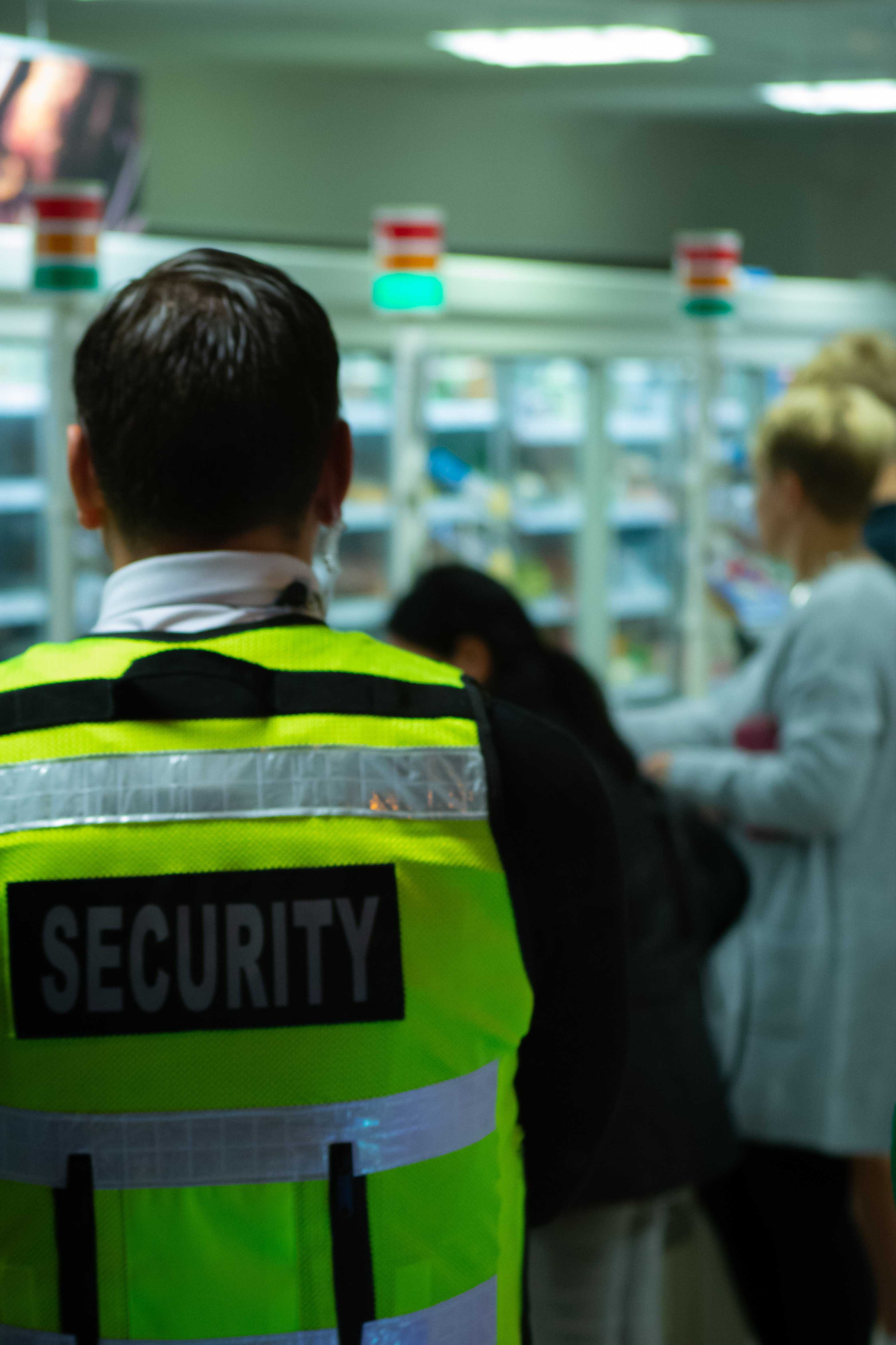 A Security Guard in a neon yellow vest looking at a room with people looking at products