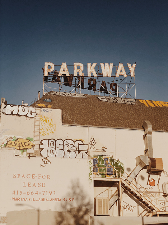 A sign reading "parkway" in Oakland California. Lots of graffiti can be seen on the back of a building.