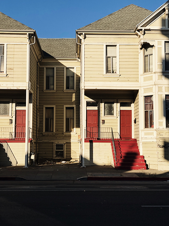 The outside apartments. The building has broken windows and trash outside of it.
