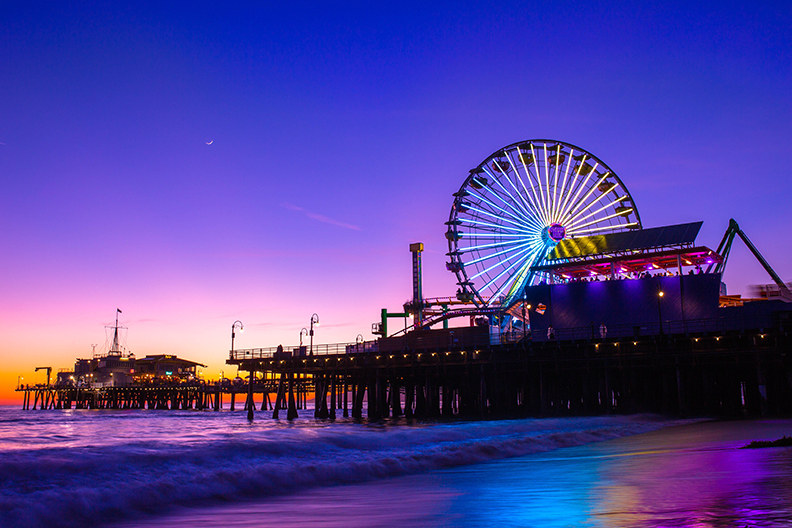 Santa Monica Pier at sunset. Lights on the ferris wheel are lit up.