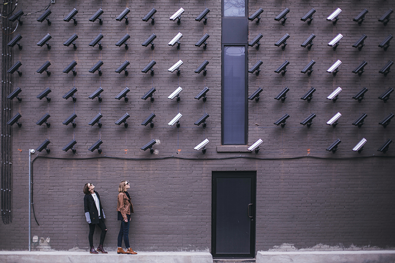 Instead of an 8 camera security system there is a wall of over 60 cameras with two bystanders looking up at them.