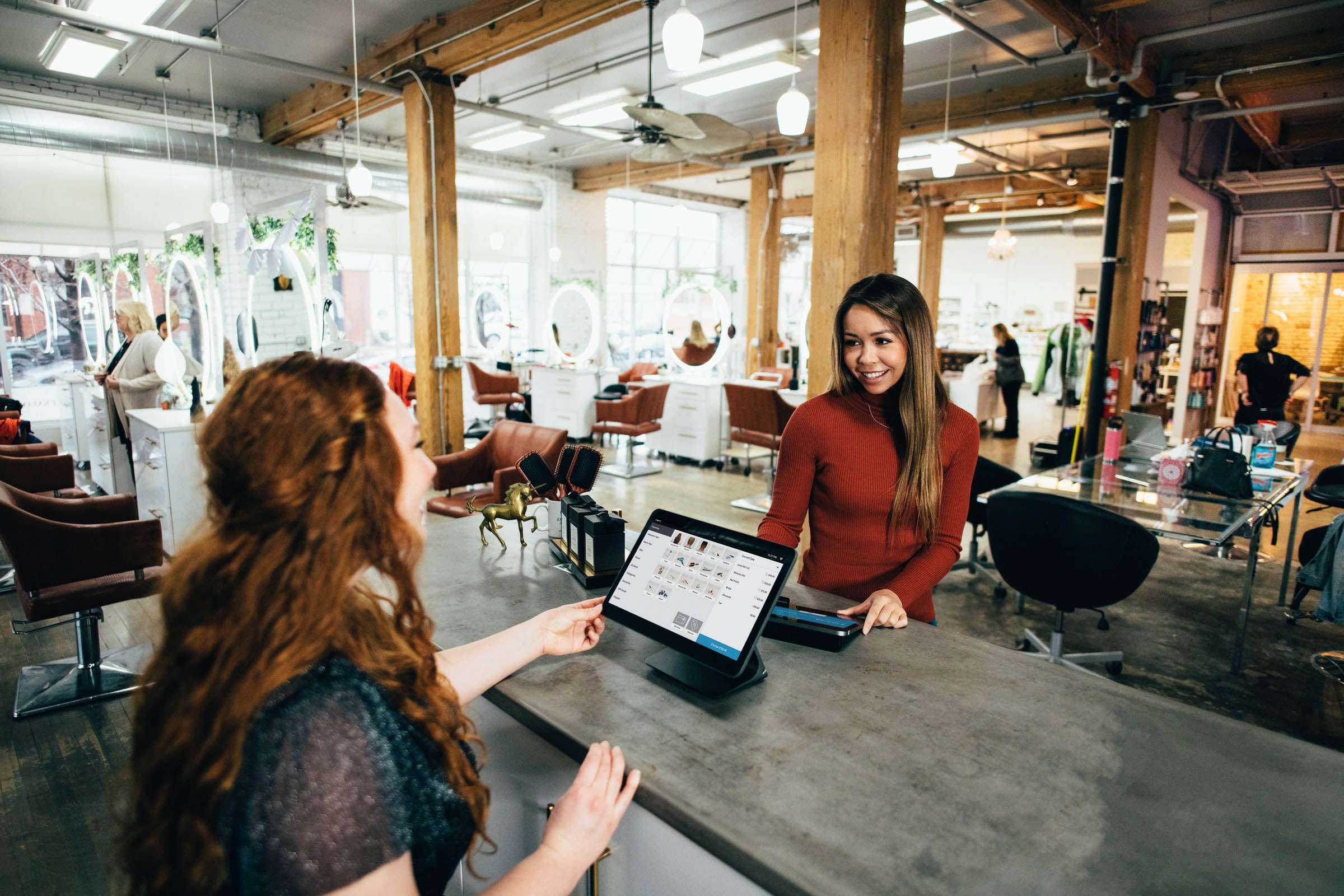 Two woman talking with a desk between them in a salon