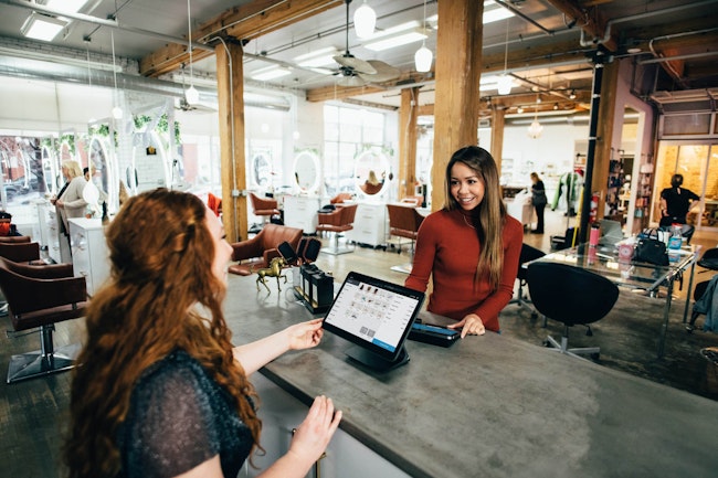 Two woman talking with a desk between them in a salon