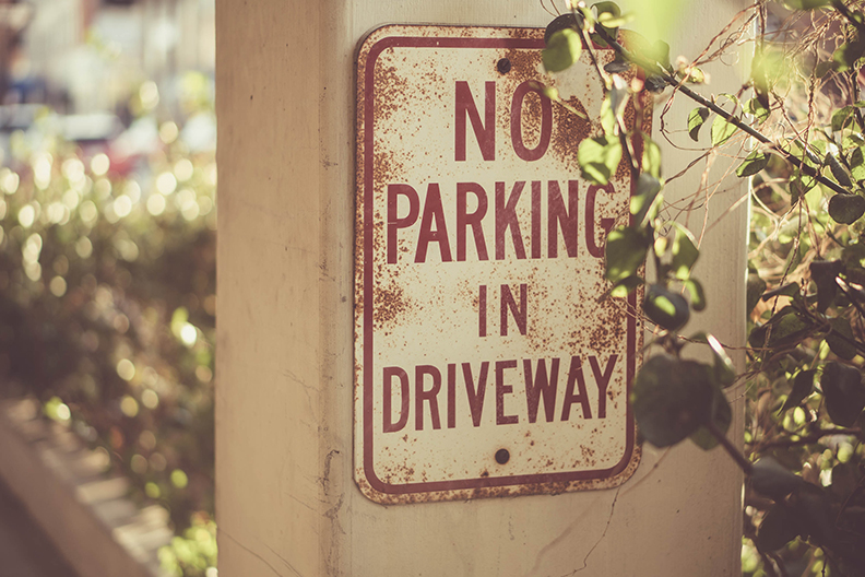 No Parking in Driveway Sign that is starting to rust and is slightly blocked by a branch