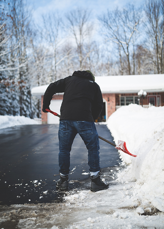 Man shoveling snow out of his long driveway in winter.
