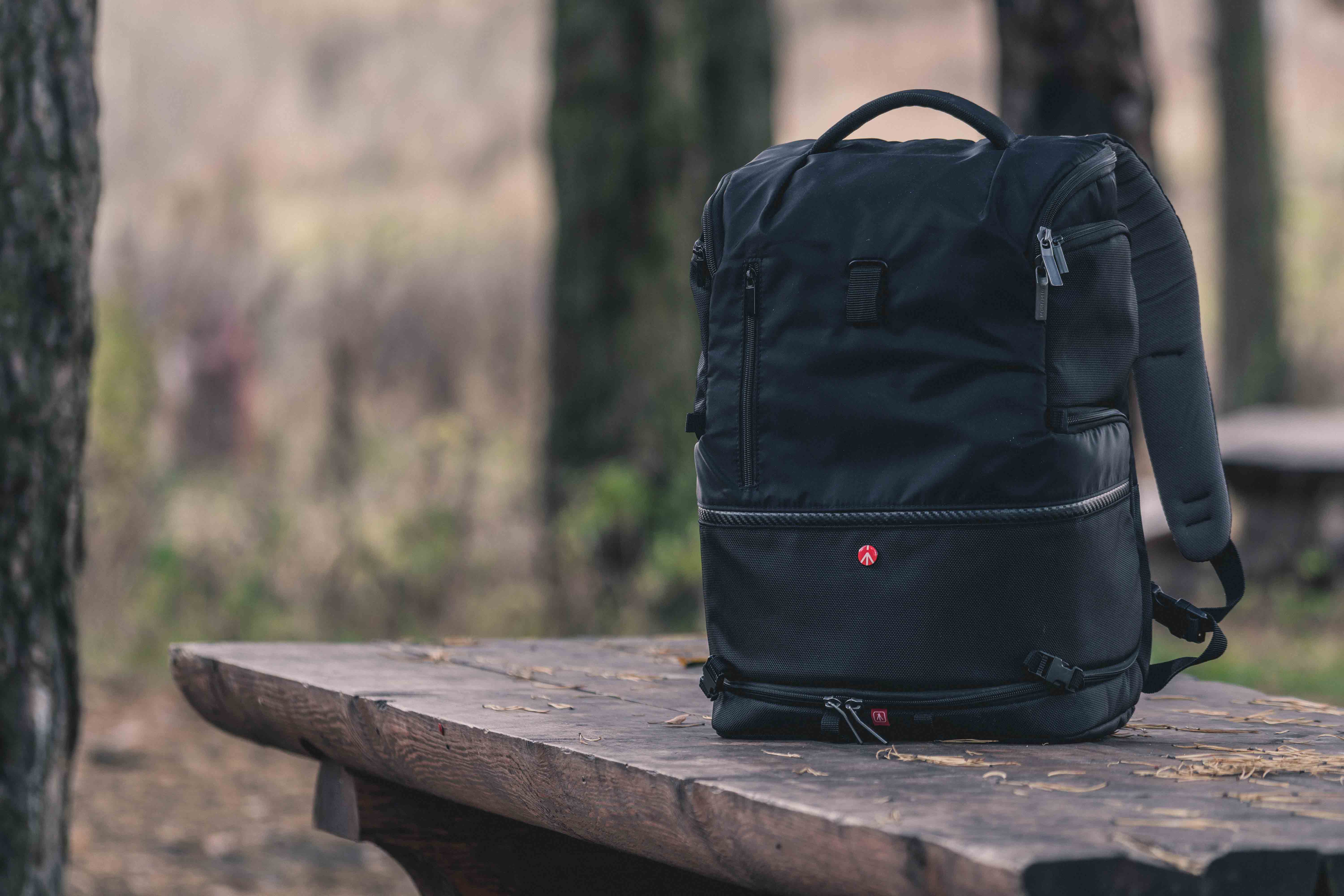 A black backpack atop a wooden bench with woods in the background