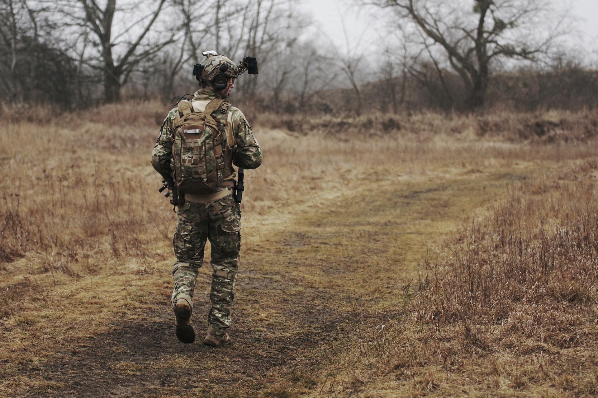 A soldier walking through a dry field on an overcast day.