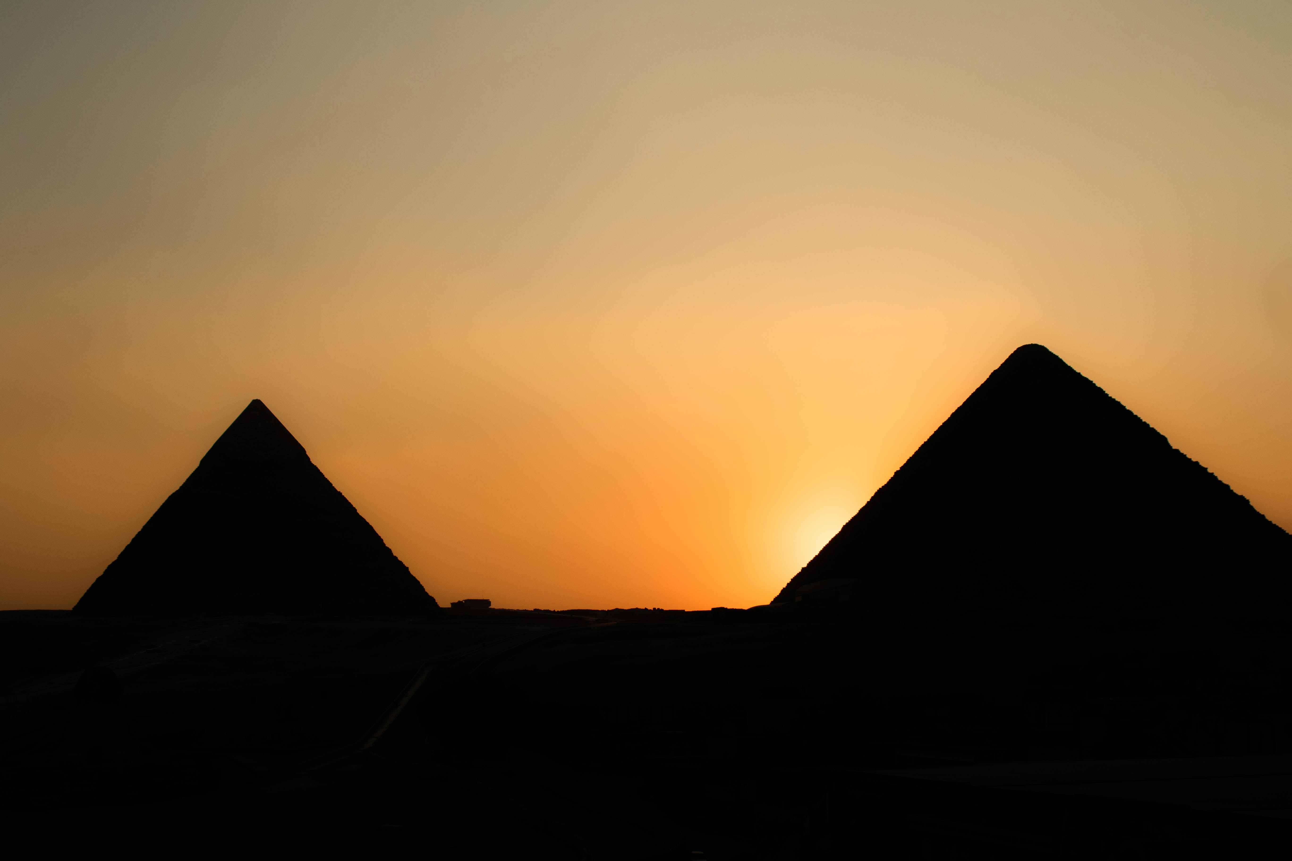 Two Egyptian pyramids dark with the sun setting behind them