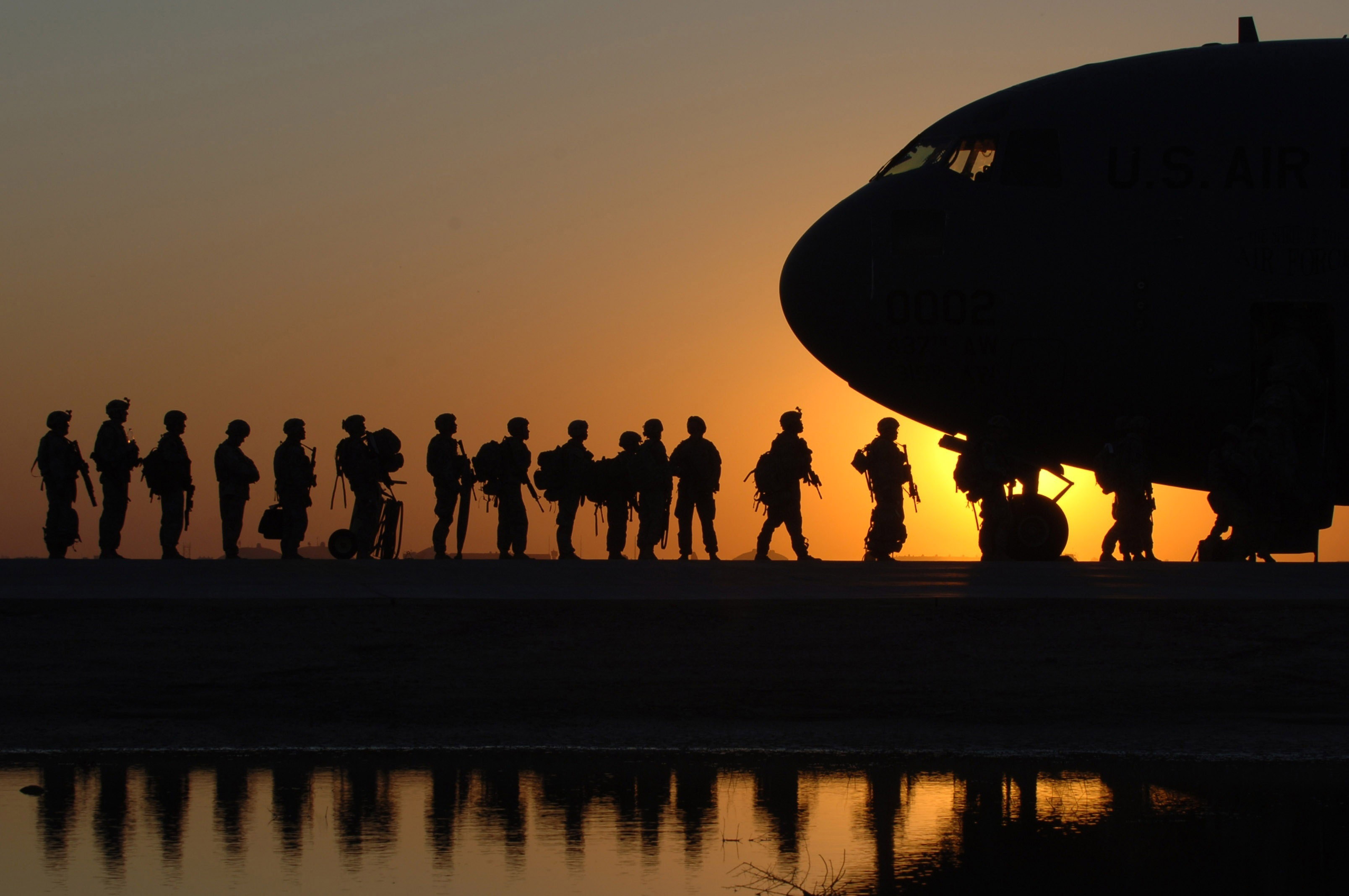 Multiple soldiers lined up to enter a large airplane with sunset behind them