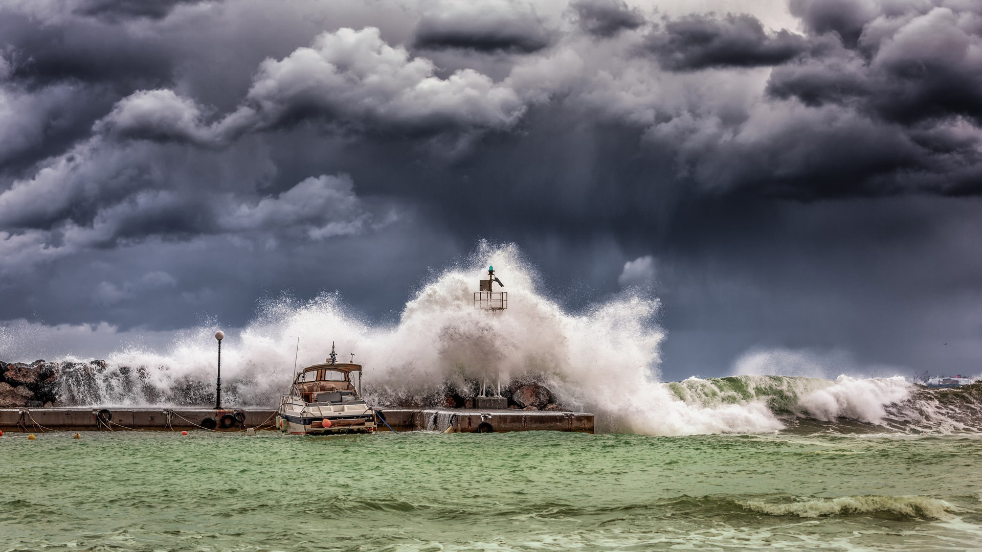 A large wave crashing over a dock with dark clouds in the background