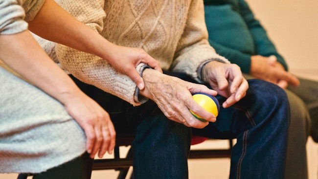A woman holding an elderly mans arm whose hand is gripping a stress ball