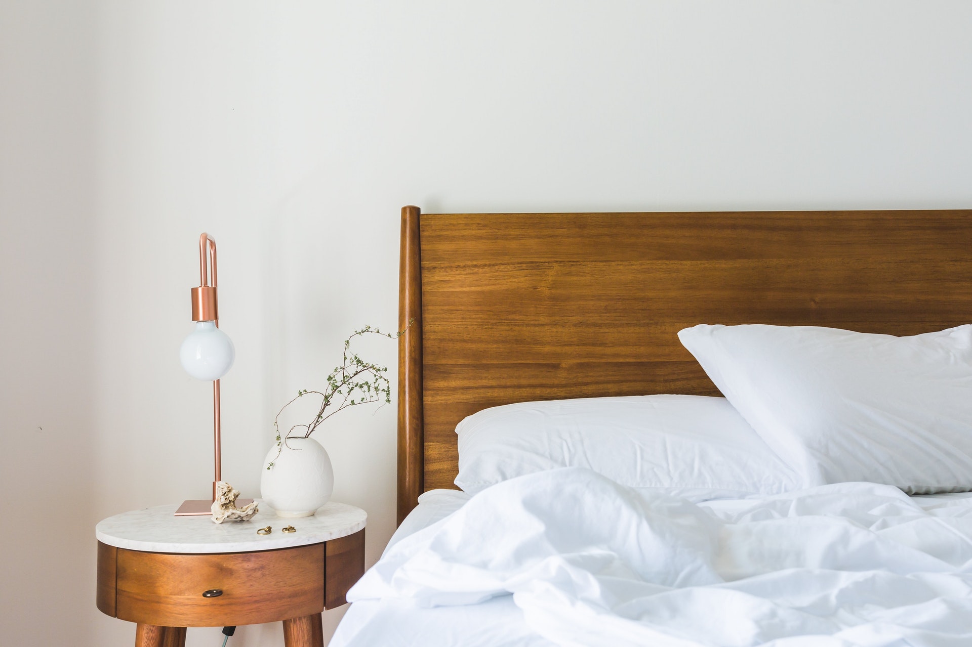 A bed with rumpled white sheets a wooden headboard and a small desk alongside it