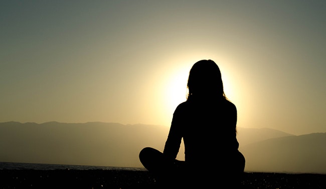 Silhouette of a person sitting at peace while they stare towards the sun.