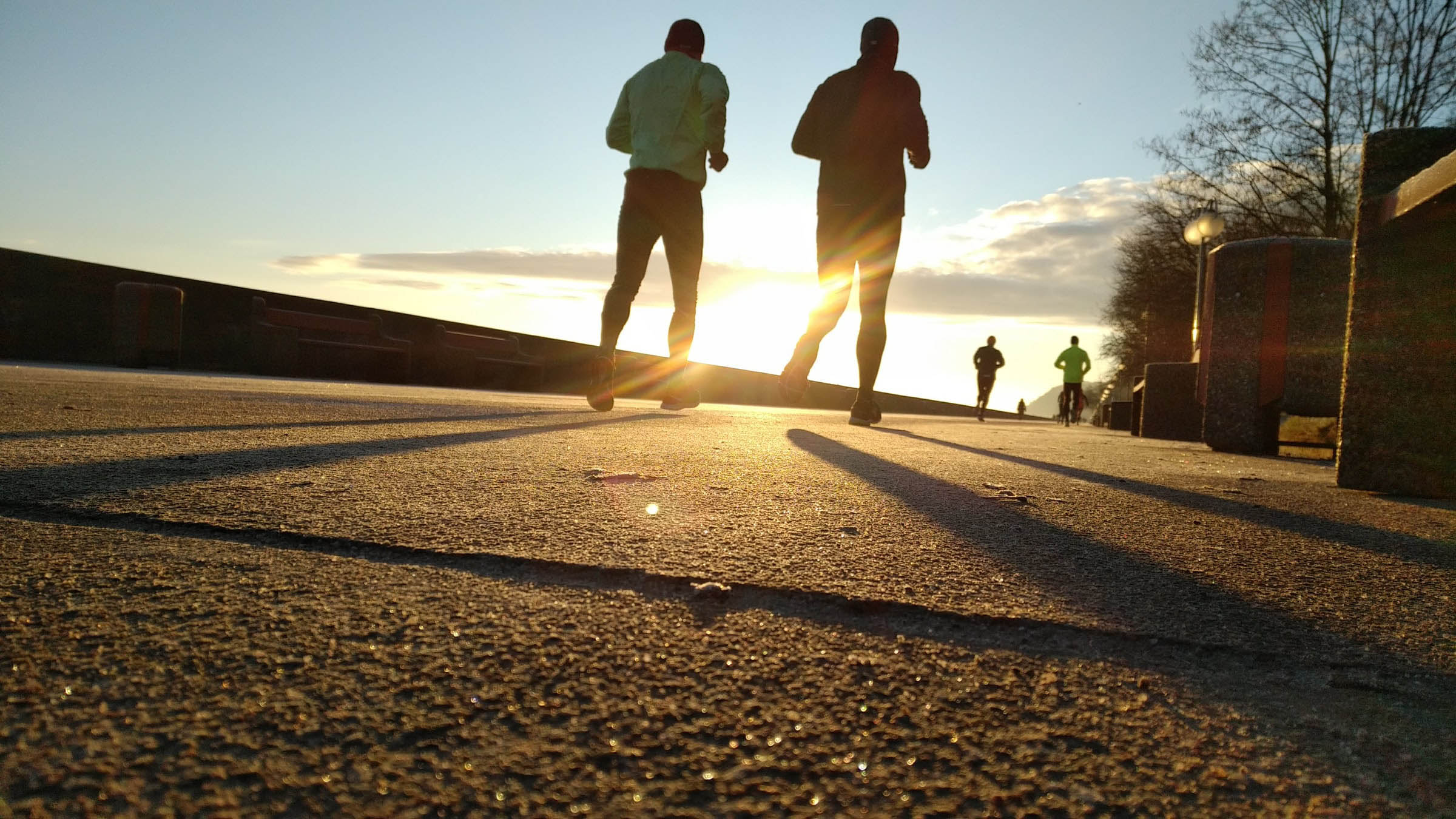 Two joggers running towards the sunrise on a concrete sidewalk
