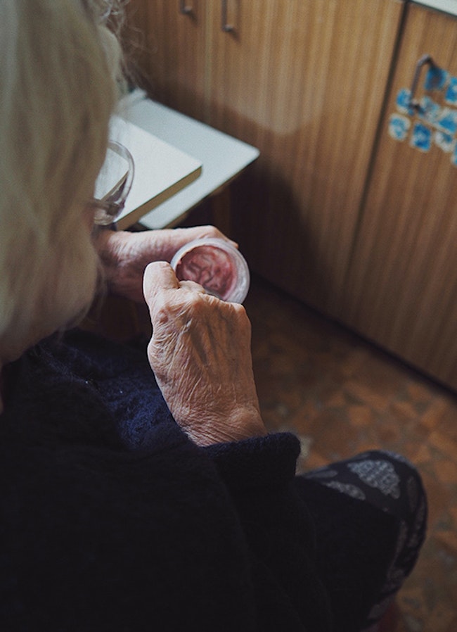 An old woman eating in her kitchen.