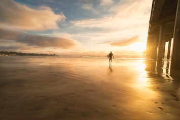 Surfer Walking Near Pier in San Diego at Sunset