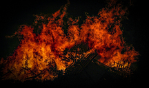 Inferno burning branches and pallets of wood at night.