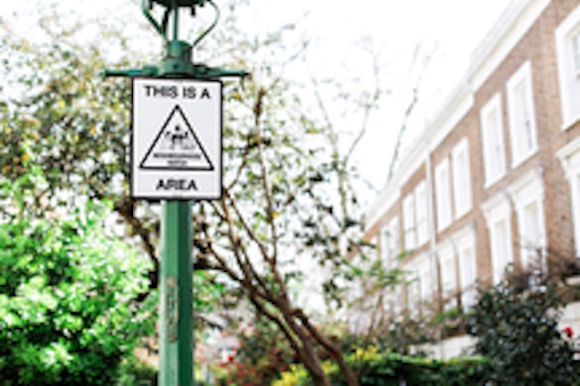 Neighborhood watch sign on green lamp post. Trees and a home can be seen in the background.