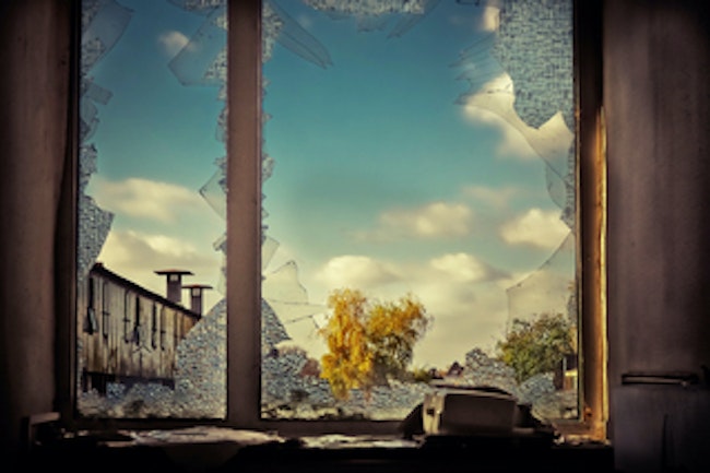 Broken Window. Outside can be seen a line of apartments, some trees, and the blue sky with a few clouds in it. 