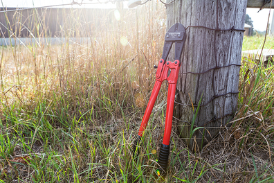 Bolt cutters used for opening padlocks lying against a wooden fence post on a sunny day.