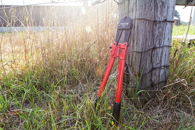 Bolt cutters used for opening padlocks lying against a wooden fence post on a sunny day.