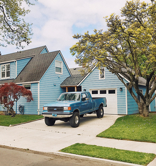 A blue truck in the driveway of a blue house. 