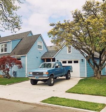 A blue truck in the driveway of a blue house. 