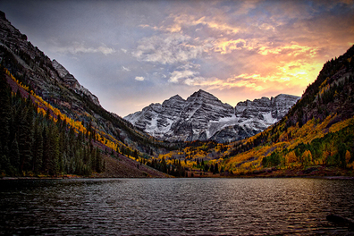A Lake surrounded by autumn-leaved trees in Colorado. A snow covered mountain in the background.