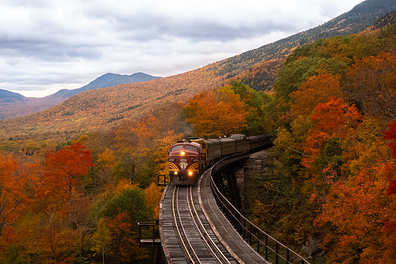 Train running through a red forest in New Hampshire during fall.
