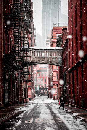 Fire Escape in a Snow Storm. A walking bridge connects two red buildings.