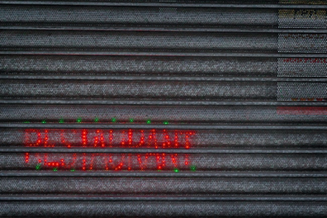 Security shutters with light up restaurant sign shining through the little holes in the security shutters.