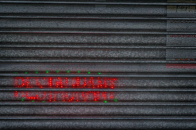 Security shutters with light up restaurant sign shining through the little holes in the security shutters.